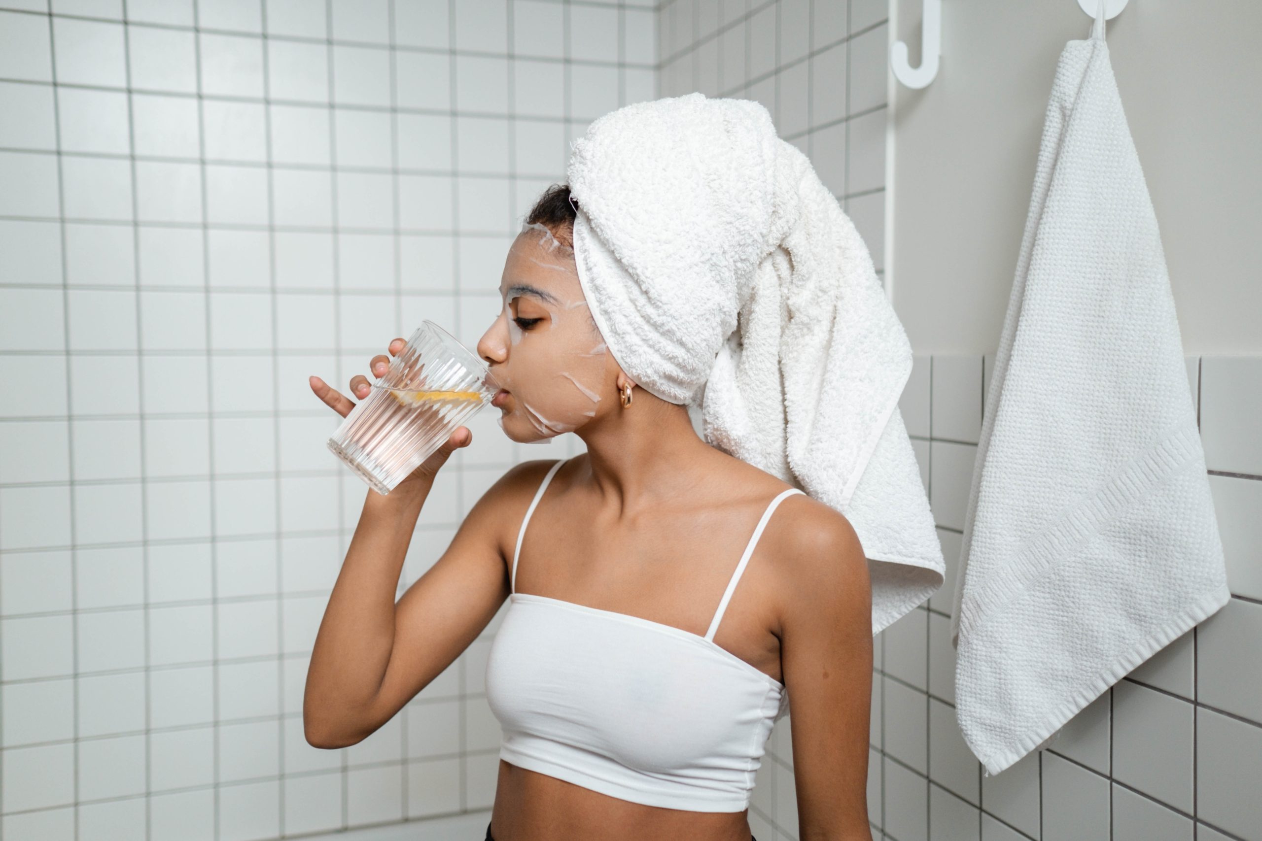 jeune femme qui boit un verre d'eau pendant son masque visage